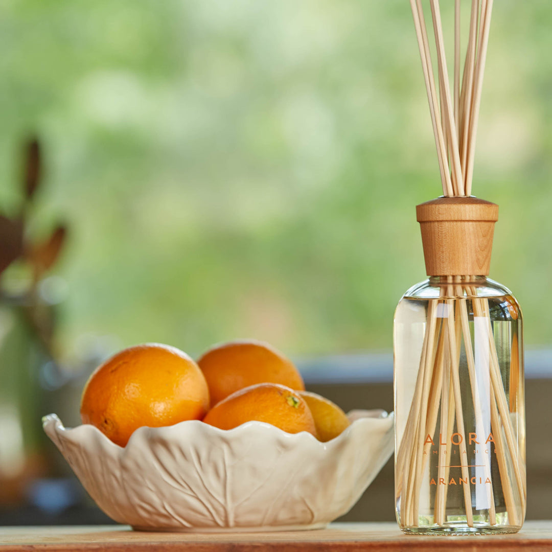 Arancia reed diffuser next to a cream-colored bowl filled with oranges