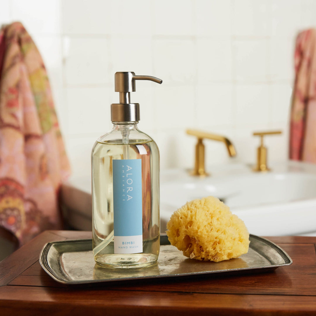 Bimbi hand wash bottle sites on a silver tray next to a sponge in a bathroom.