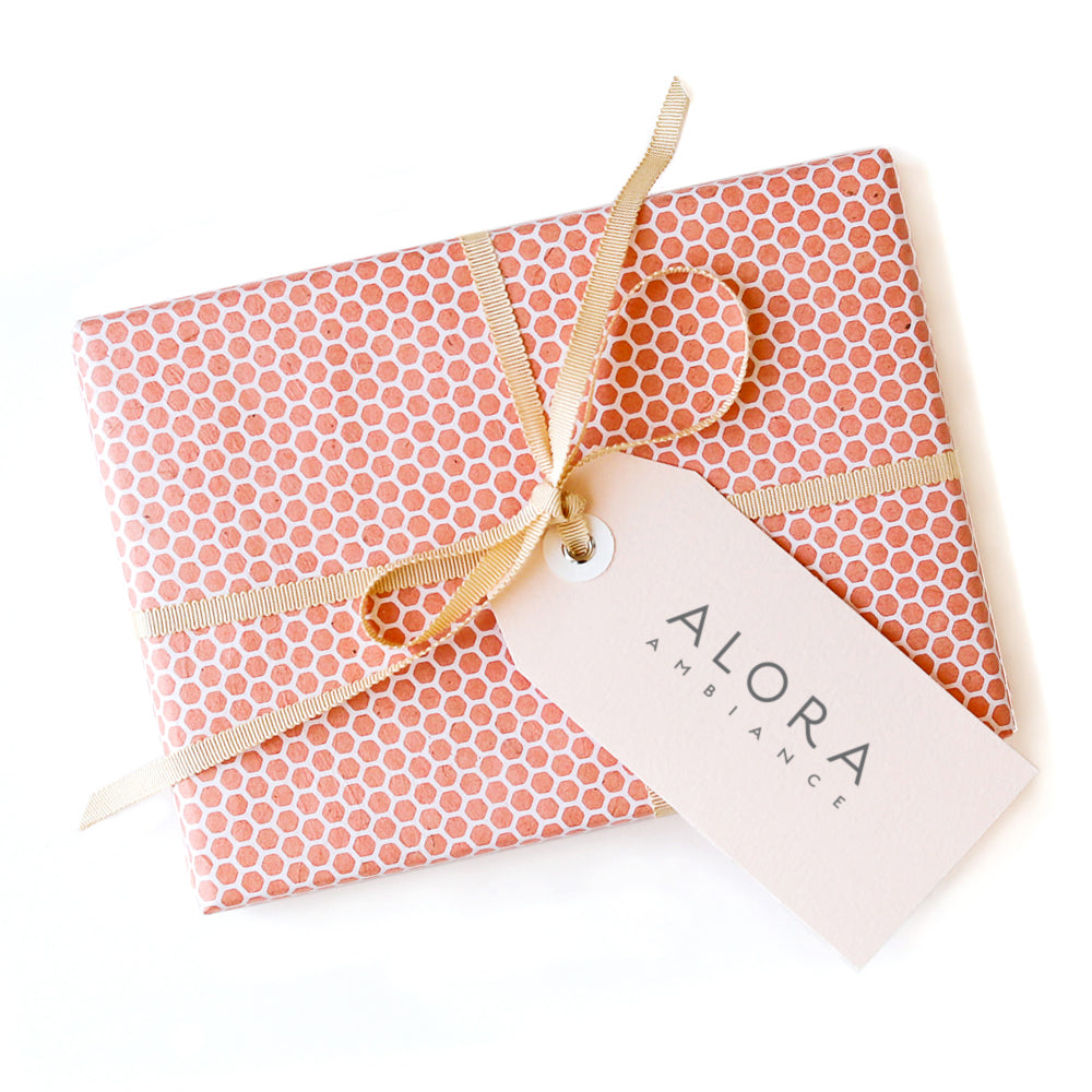 Small box wrapped in pink hexagonal wrapping paper, tied with a pink ribbon and a tag that says "Alora Ambiance"