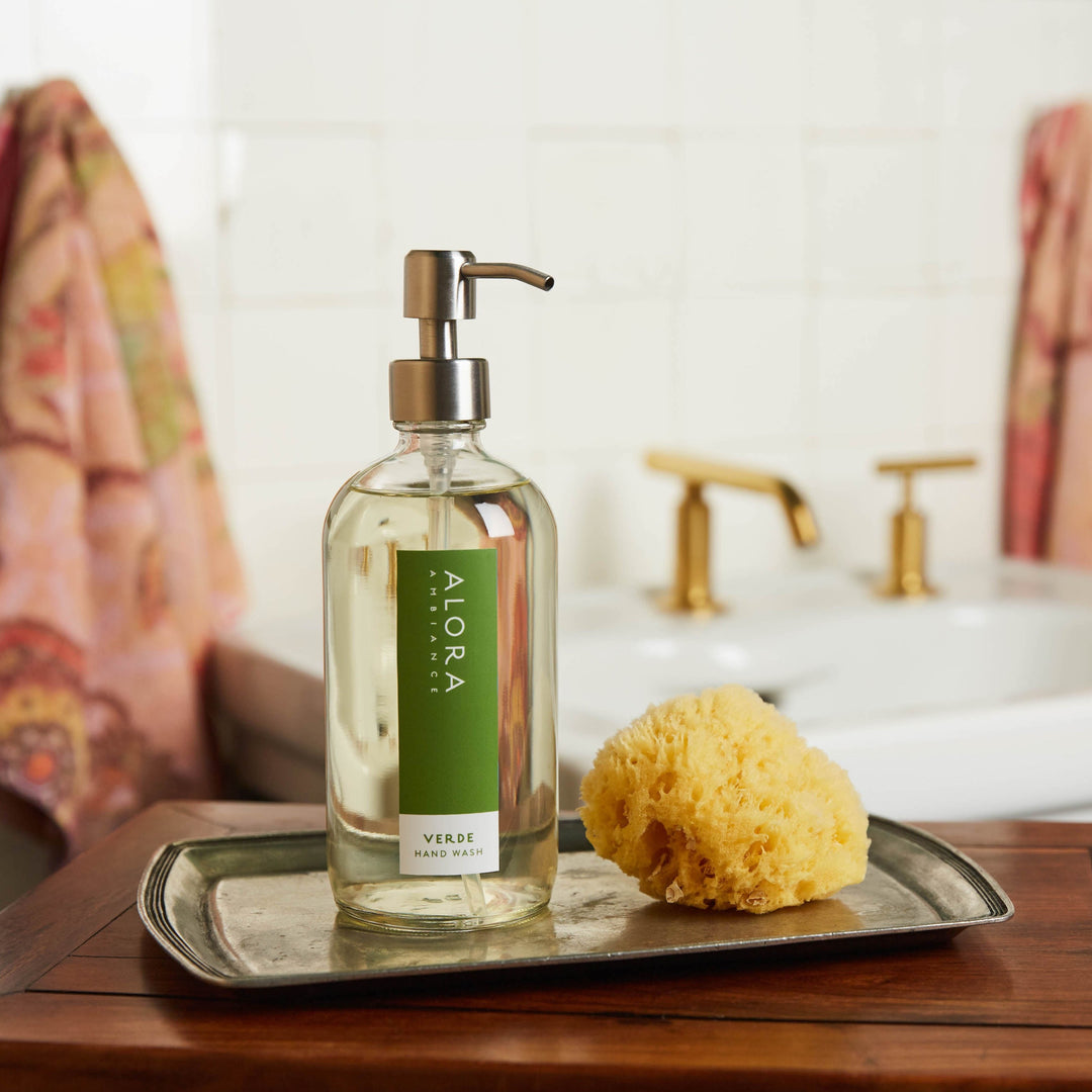 Verde hand wash bottle on a small silver tray in a bathroom in front of a sink.