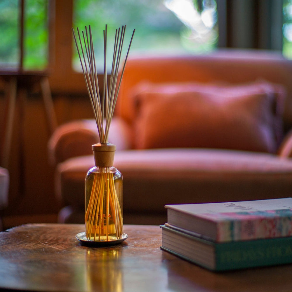 Reed diffuser sitting on a coffee table next to two books with a red chair in the background